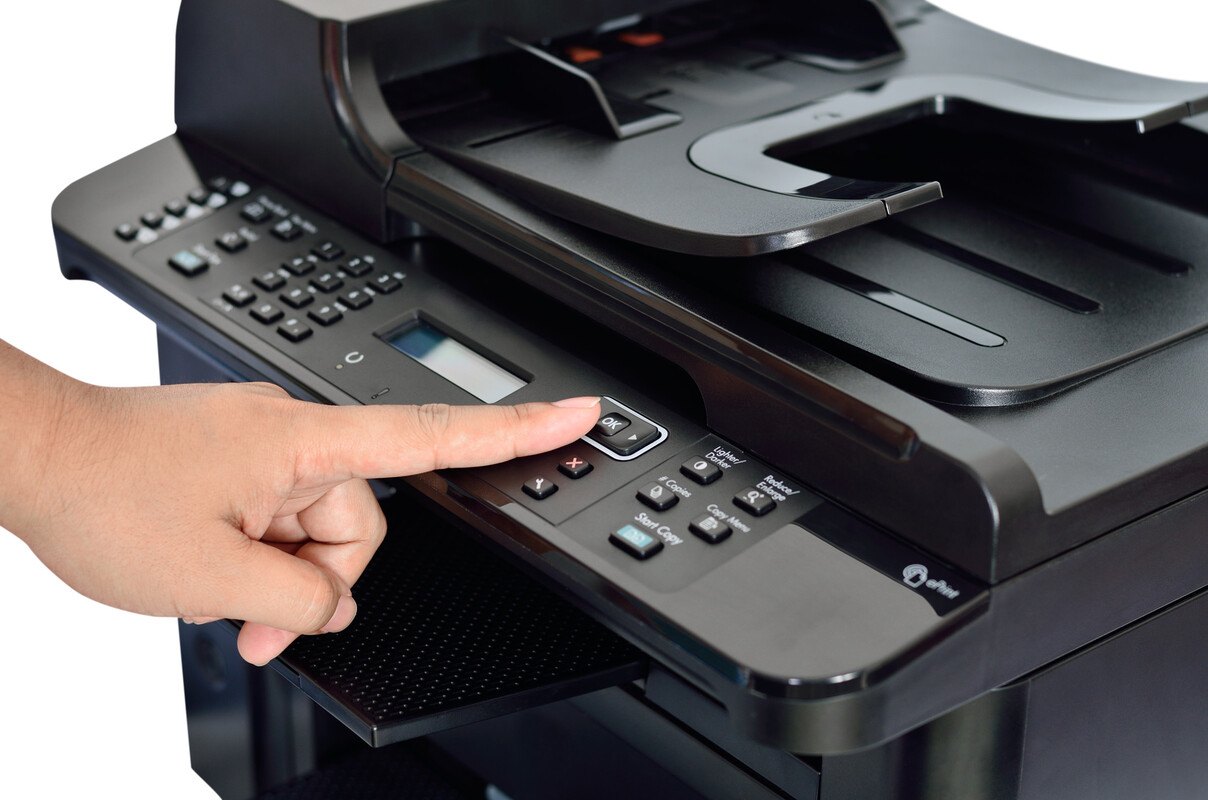 Dito che preme il tasto OK di una stampante multifunzione nera con alimentatore documenti, display e tastierino numerico